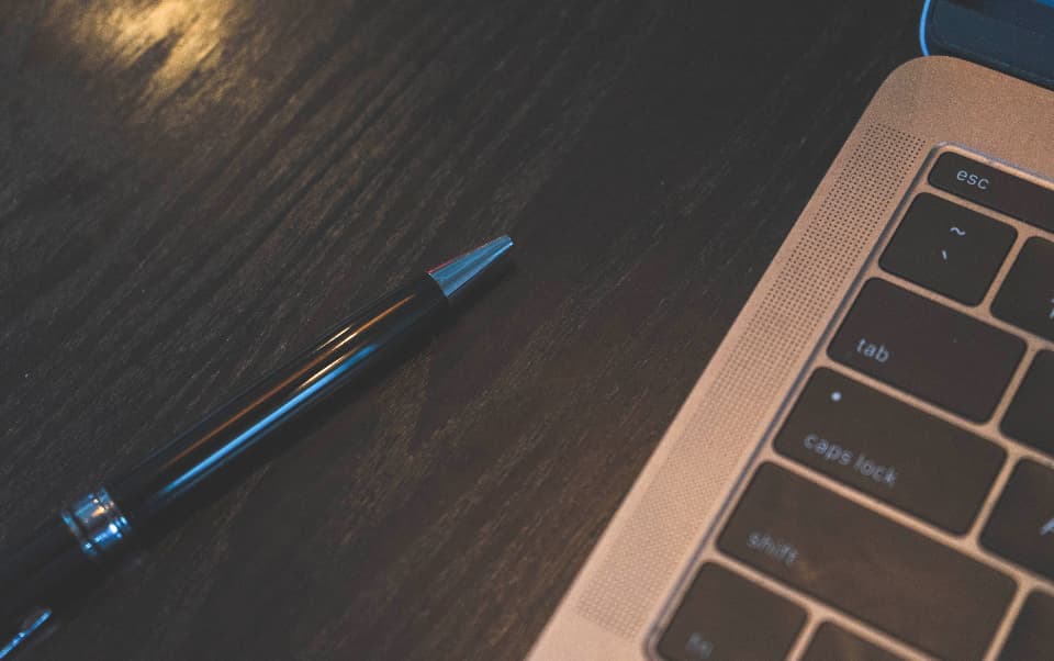 Close-up of a laptop keyboard and a pen on a dark desk