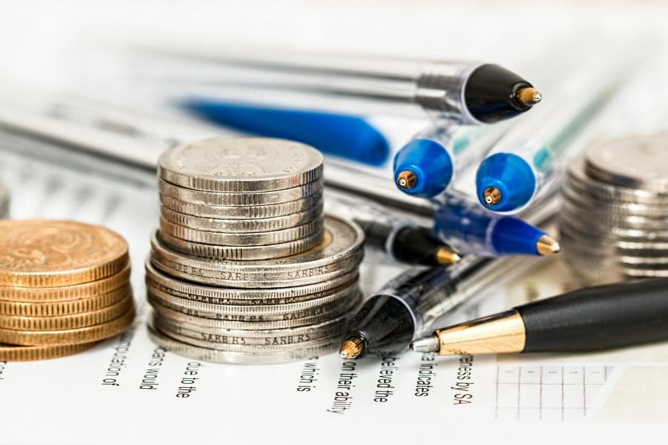 Stacks of coins next to a row of pens on a printed page