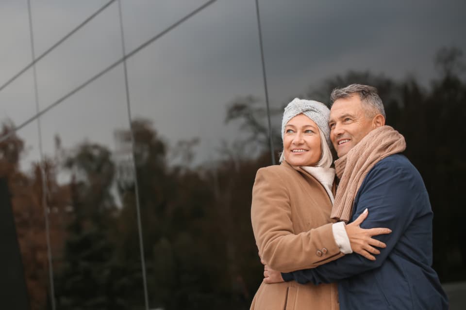 Smiling older couple in winter coats and scarves standing together outside a glass building