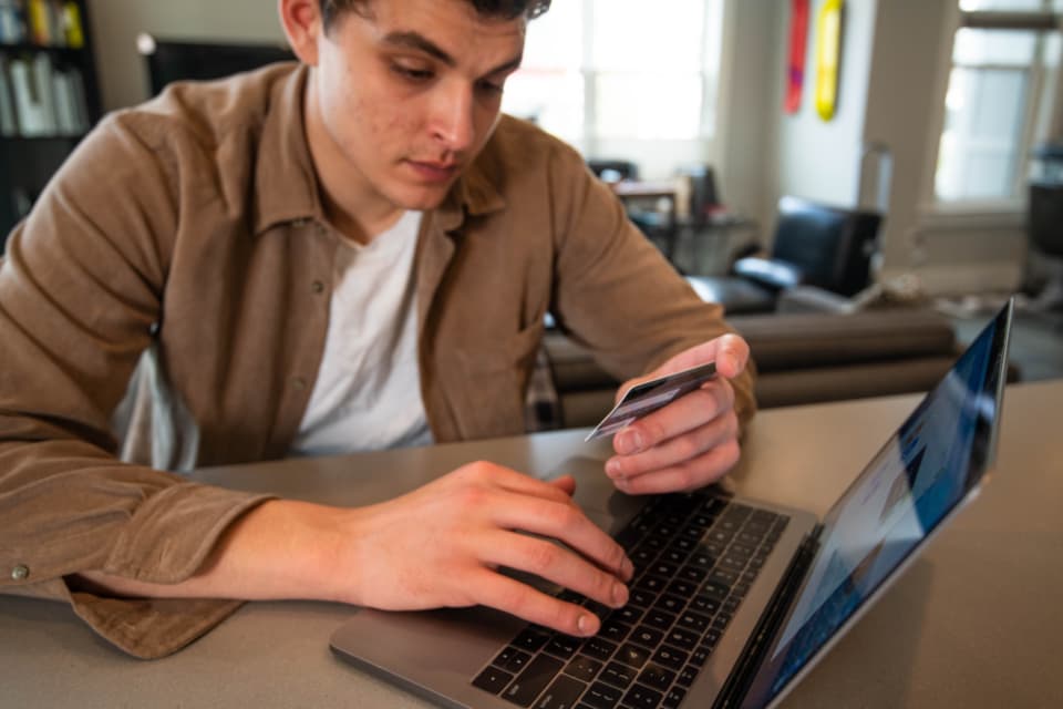 Hands holding a credit card in front of a laptop while shopping online