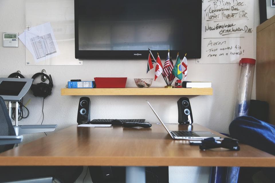 Desk with a laptop, speakers and a television in a bright office