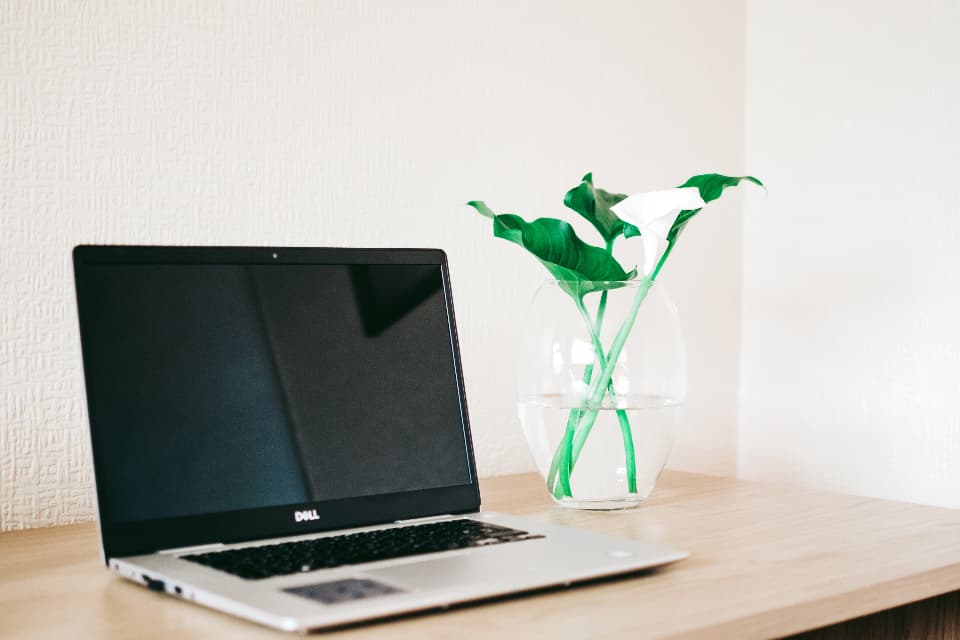 Open laptop on a clean white desk next to a vase of flowers